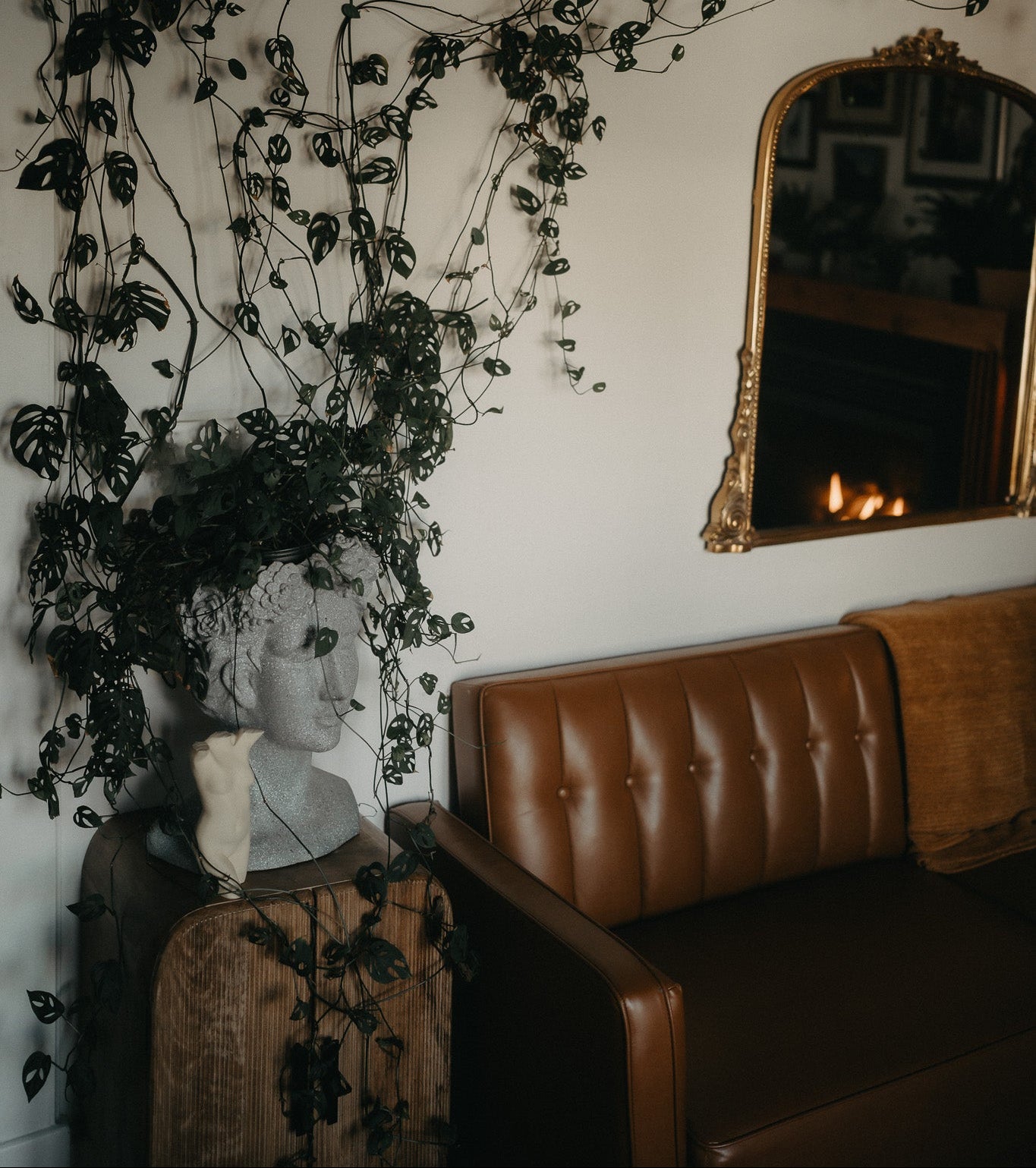 Living room with brown leather sofa, decorative mirror, and plant decorations.